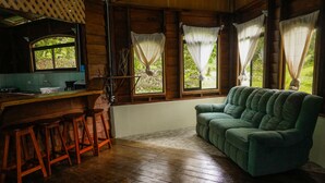 Une pièce chaleureuse avec un bar en bois, un canapé vert et une fenêtre avec des rideaux.
