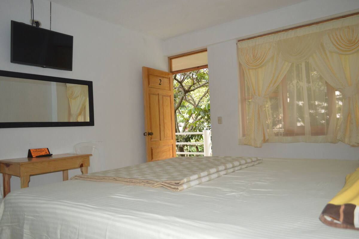 Une chambre à coucher avec un lit, un bureau en bois, un miroir et une porte donnant sur un balcon.