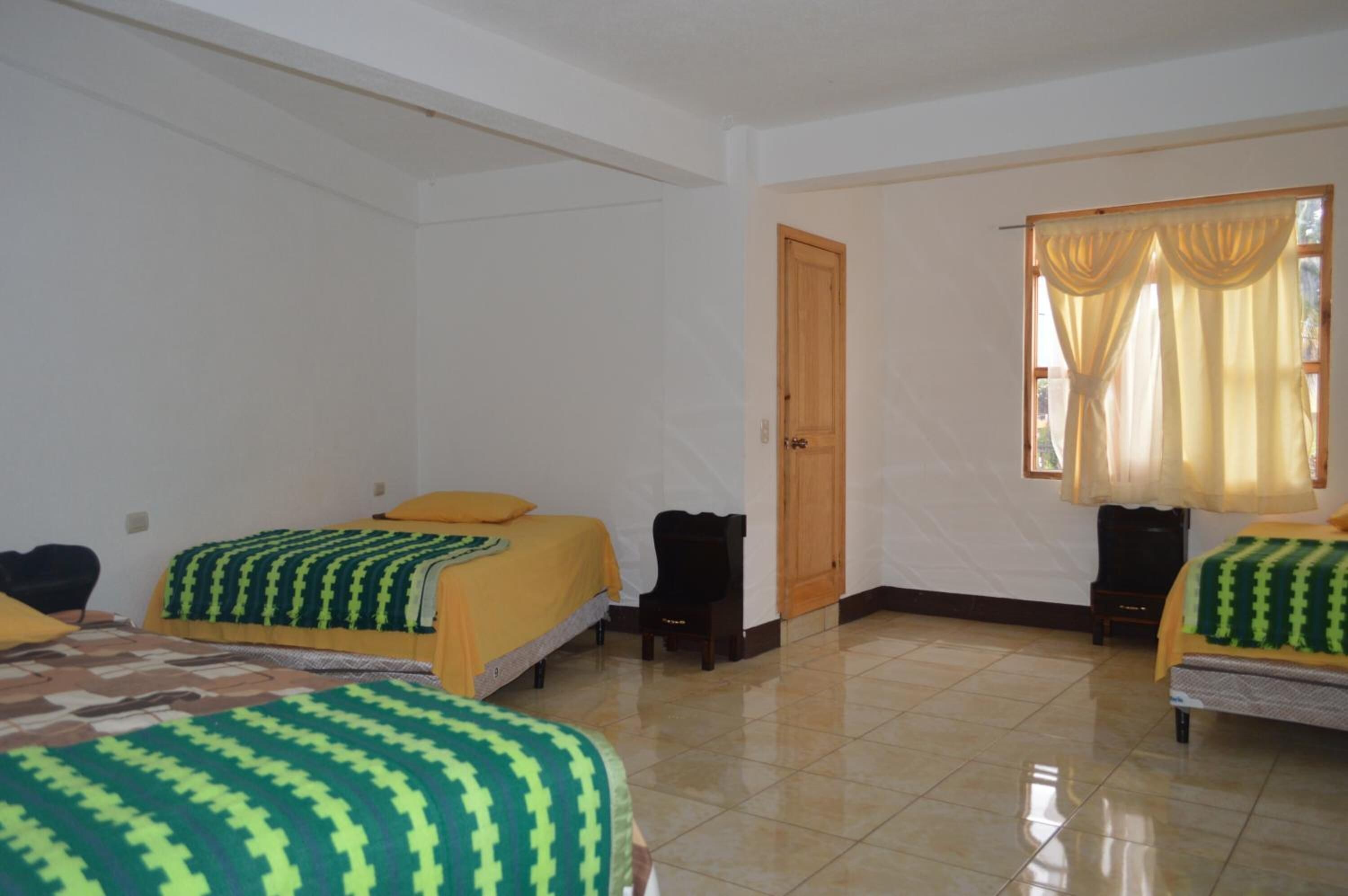 Habitación de hotel con dos camas, una puerta de madera y una ventana con cortinas.