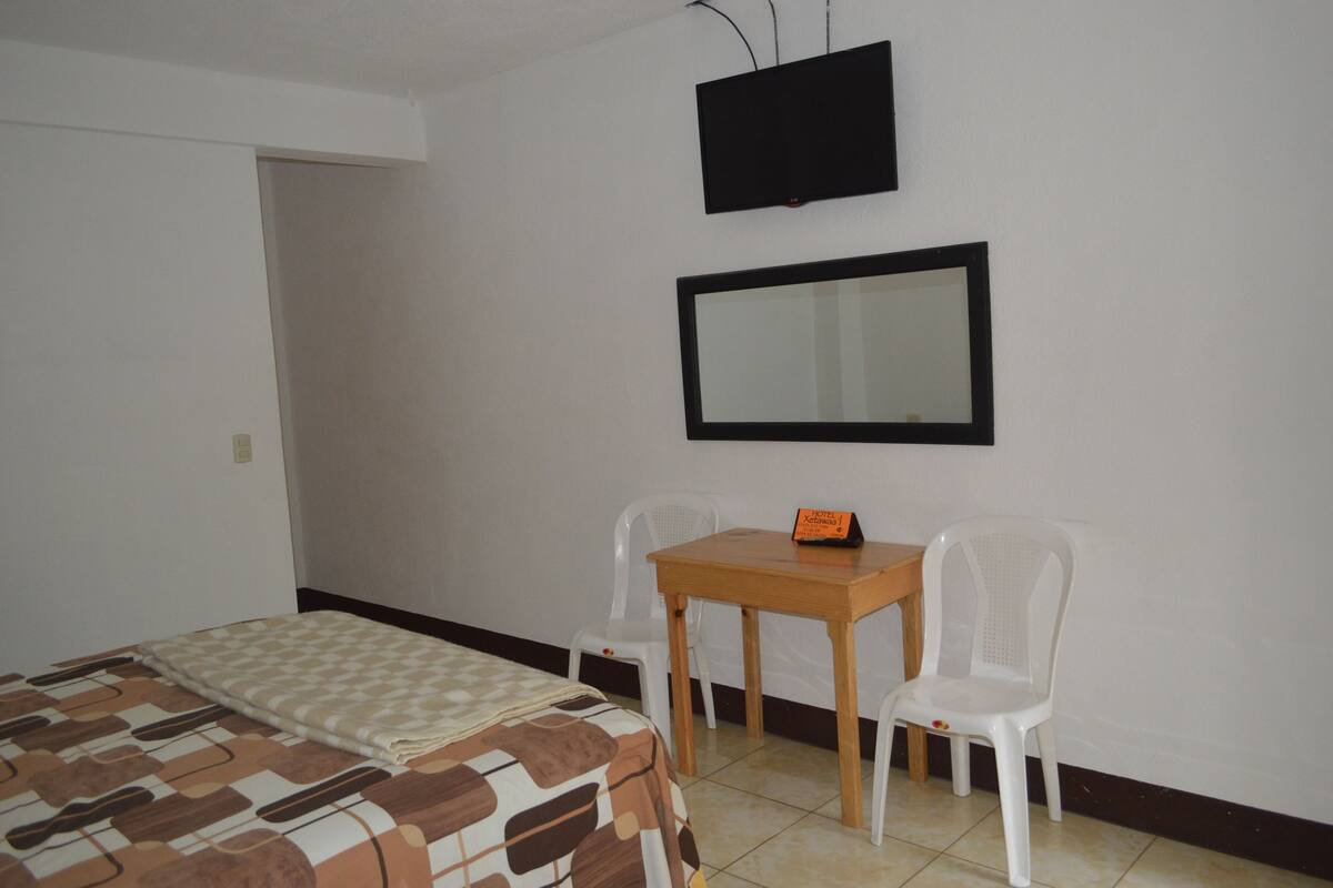 Une pièce comprenant un lit, une table avec deux chaises, un téléviseur et un miroir au mur.