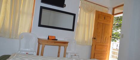 A room with a bed, a table, two chairs, a TV, and a door leading outside.