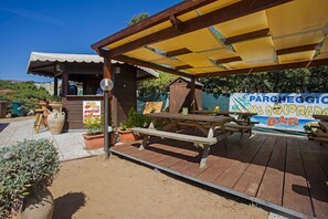 An outdoor patio area with a wooden table and benches, a small bar area, and a sign for 'PARCHEGGIO MISCELLANEO BAR'. - Playa Colorada (Gaeta)