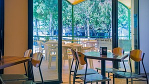 An indoor seating area with tables and chairs, large windows with a view of trees and a street outside. - Playa Colorada (Gaeta)