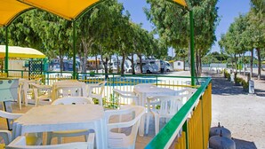 An outdoor seating area with plastic tables and chairs, a yellow canopy, and a green railing. - Playa Colorada (Gaeta)