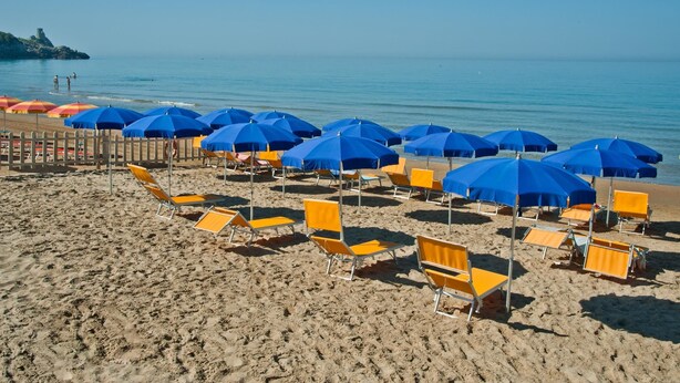 A beach with rows of yellow and blue beach chairs and umbrellas, a wooden fence, and a clear view of the sea. - Playa Colorada (Gaeta)