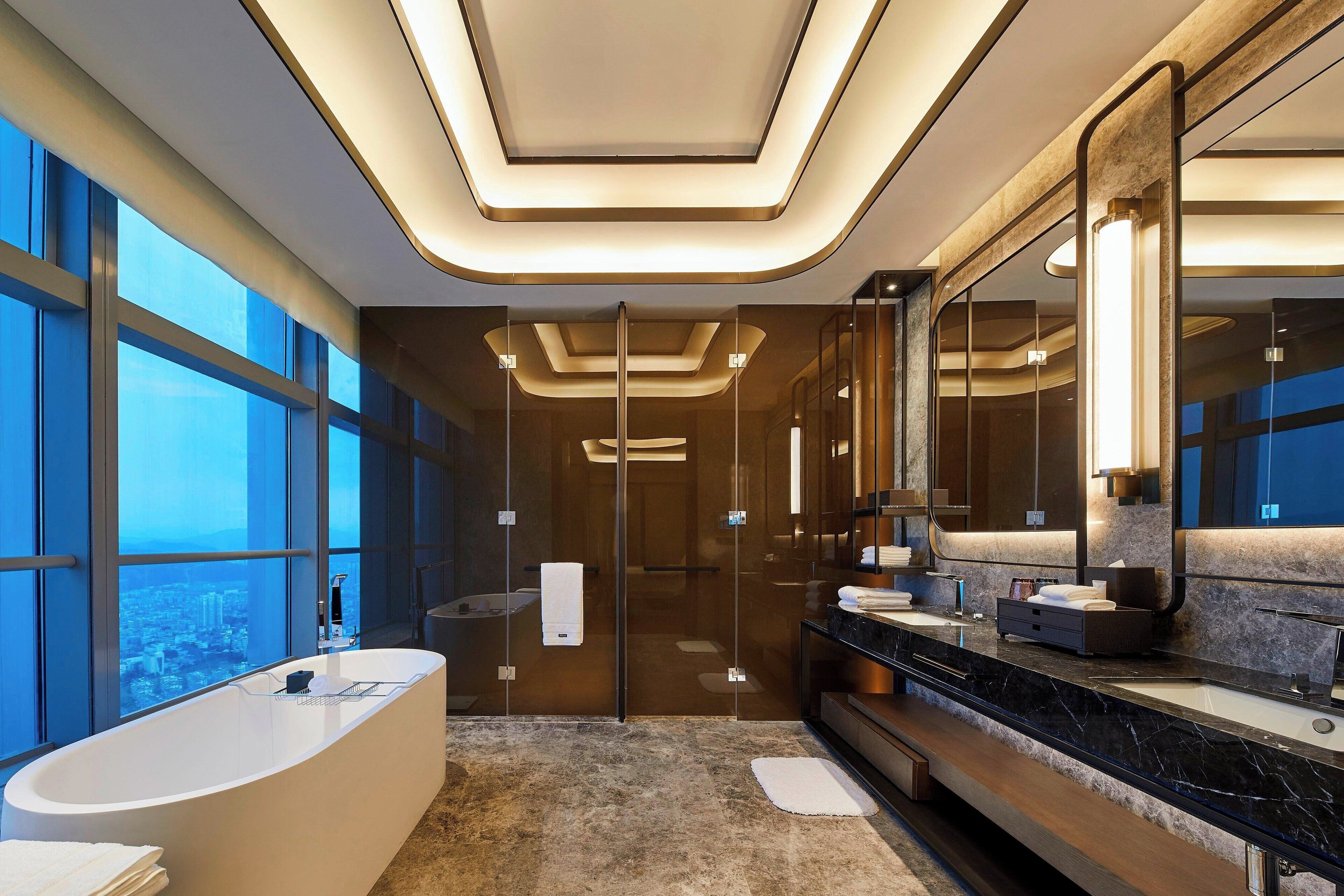 Un baño moderno con una bañera grande, un tocador con espejo y vistas a la ciudad a través de amplios ventanales.