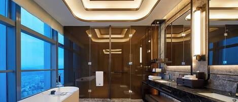 Un baño moderno con una bañera grande, un tocador con espejo y vistas a la ciudad a través de amplios ventanales.