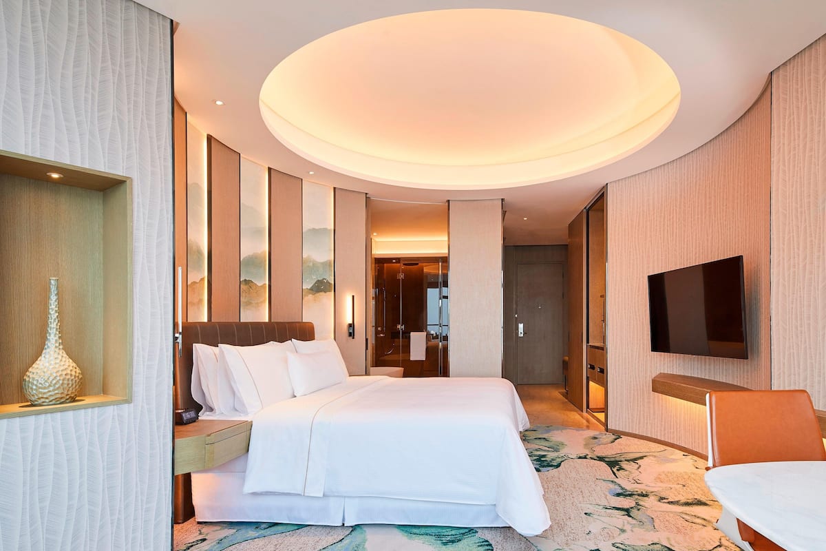 Ein Hotelzimmer mit einem großen Bett, einem flachbildfernseher an der Wand und einer dekorativen Vase auf einem Nachttisch.
