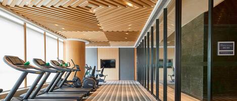 A gym with treadmills, stationary bikes, and a wall-mounted TV.