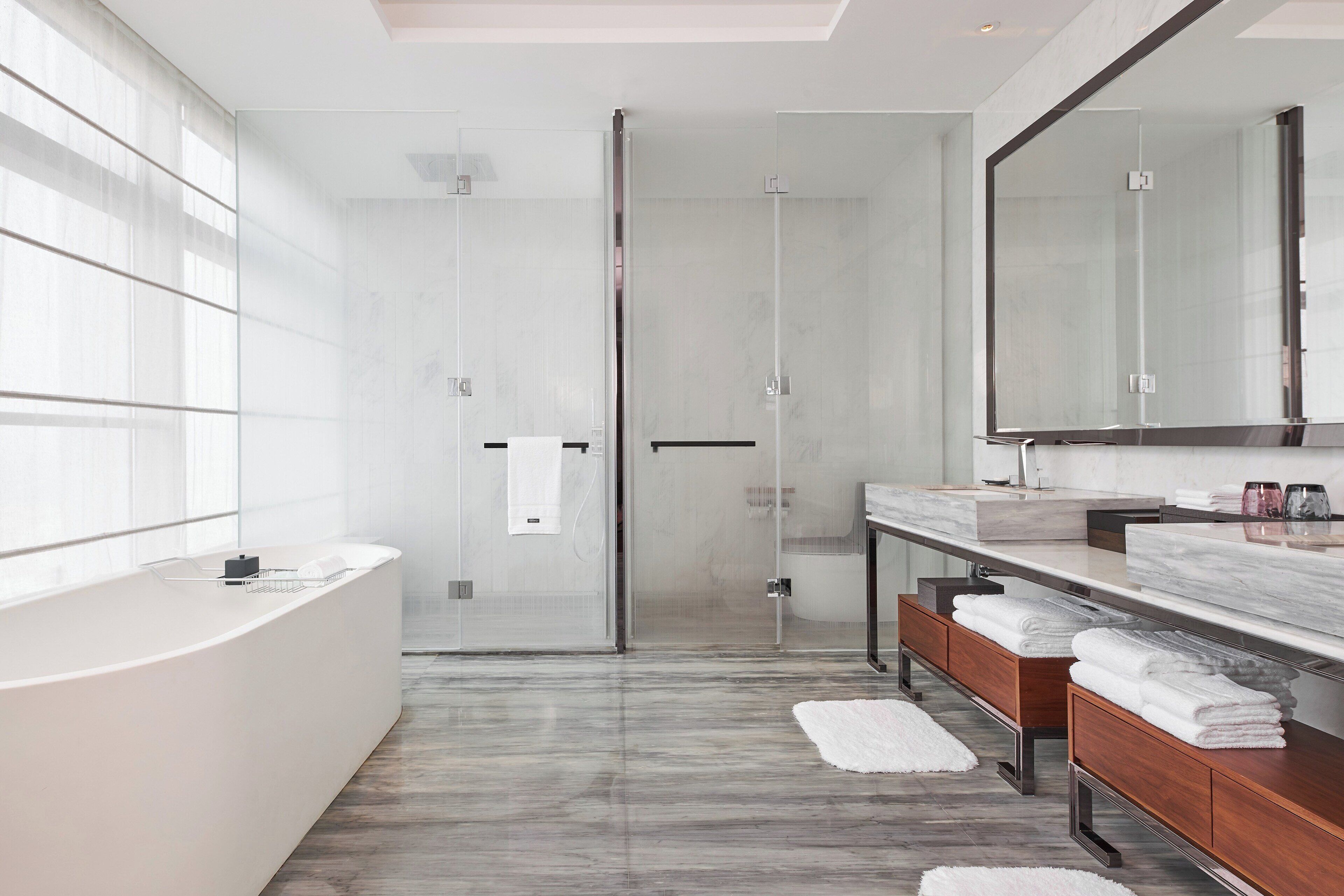 A modern bathroom with a glass shower enclosure, a large mirror, and a marble countertop.