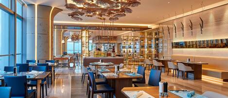 En modern restaurang med en central bardisk, högt i tak och en dekorativ taklampa.