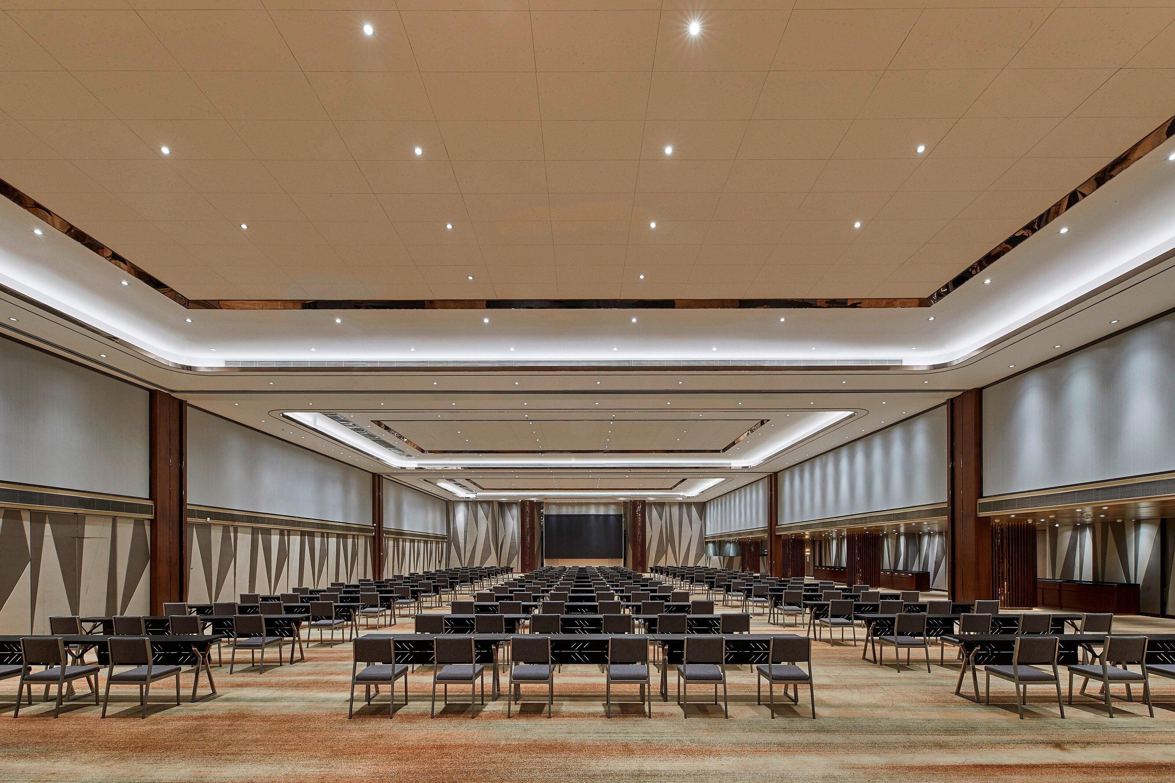 Un salón de conferencias amplio con filas de sillas, un escenario y una pantalla grande.