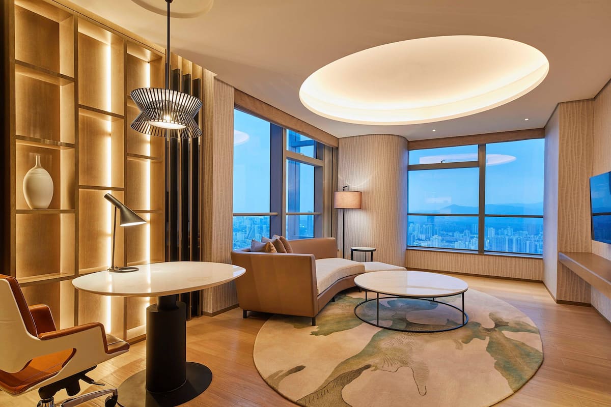Ein modernes Wohnzimmer mit einer Couch, zwei runden Tischen, einer Lampe und Blick auf die Stadt durch große Fenster.