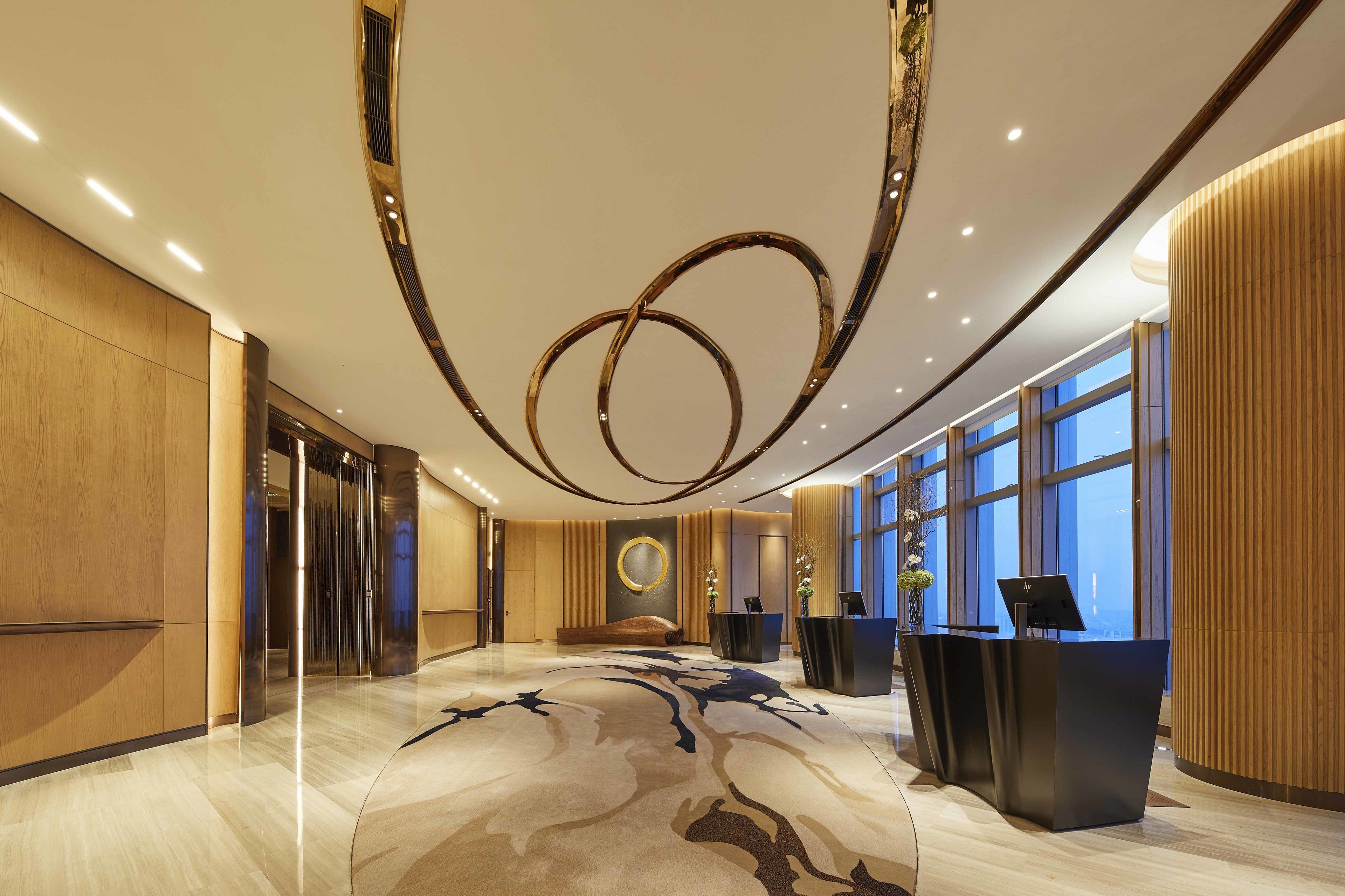 A modern hotel lobby with a marble floor, a reception desk, and large windows offering a view of the city.