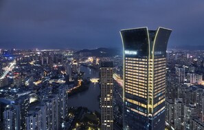 A high-rise building with the name "WESTIN" prominently displayed, surrounded by a densely populated urban area with numerous other buildings and a river. - The Westin Wenzhou (Wenzhou)