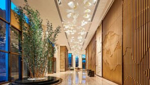 Un moderno vestíbulo de hotel con un arreglo floral central, un mostrador de recepción de madera y un techo con lámparas colgantes.