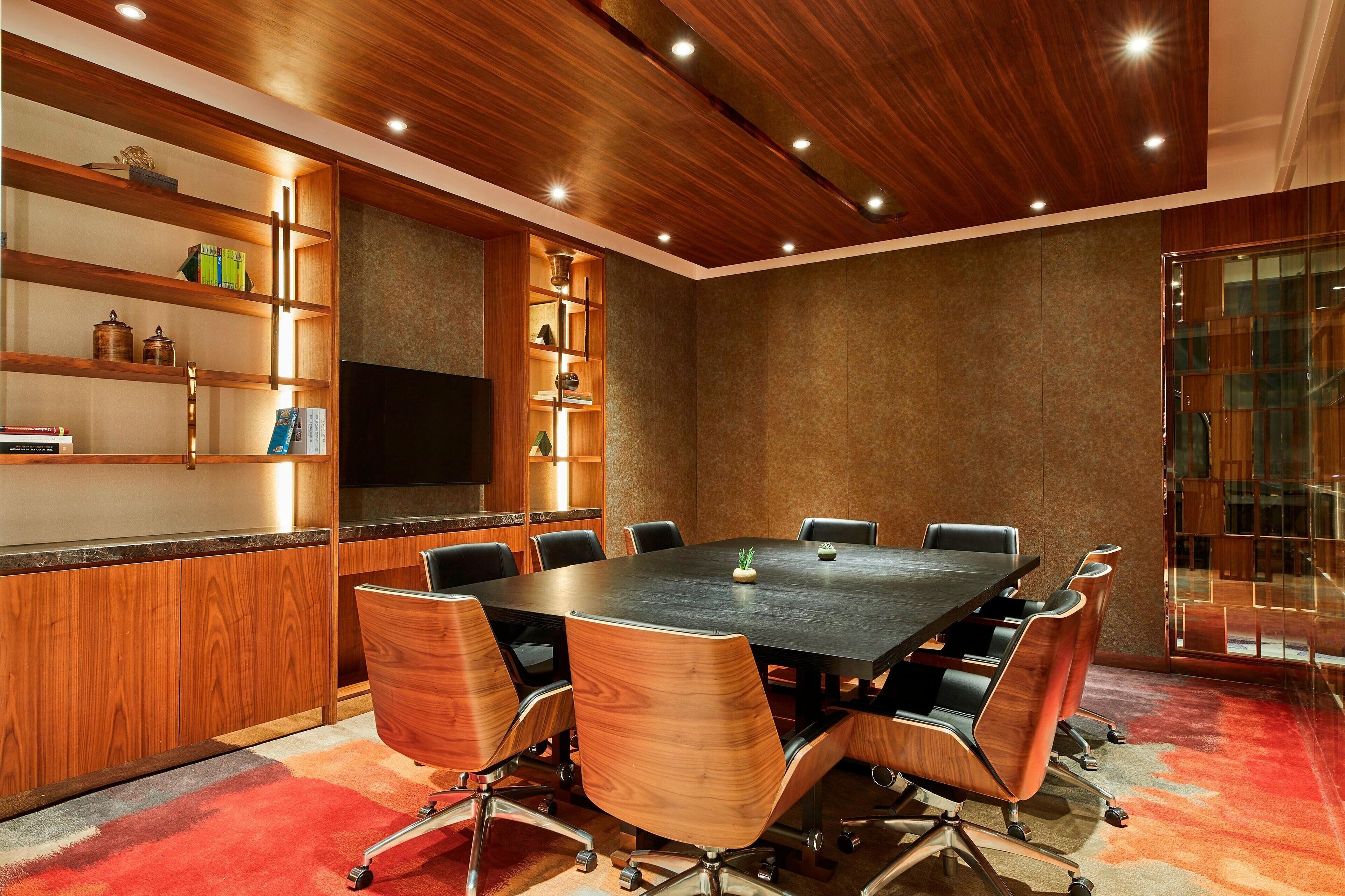 Una sala conferenze con un grande tavolo, sedie, scaffali in legno e un televisore.