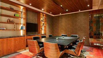 Un salón de conferencias con una mesa grande, sillas, estanterías de madera y una televisión.