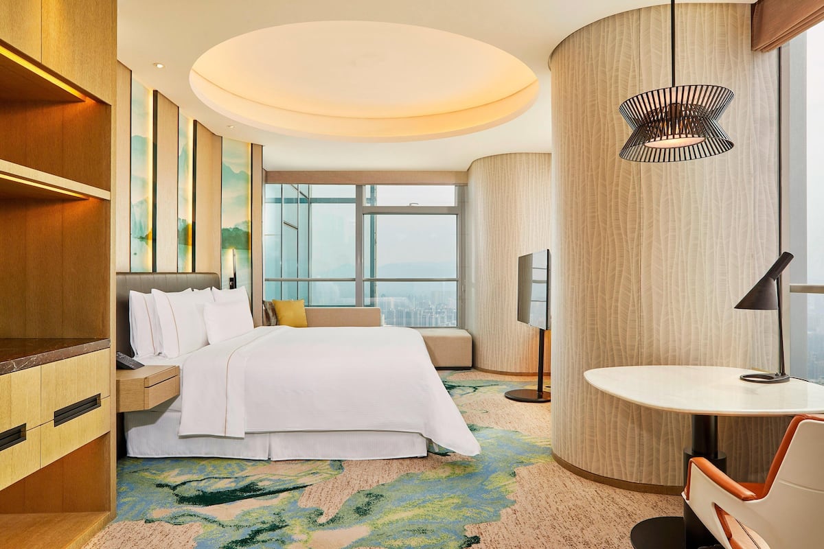 Ein modernes Hotelzimmer mit einem großen Bett, einem Schreibtisch, einem Stuhl, einem runden Tisch und Blick auf die Stadt durch das Fenster.