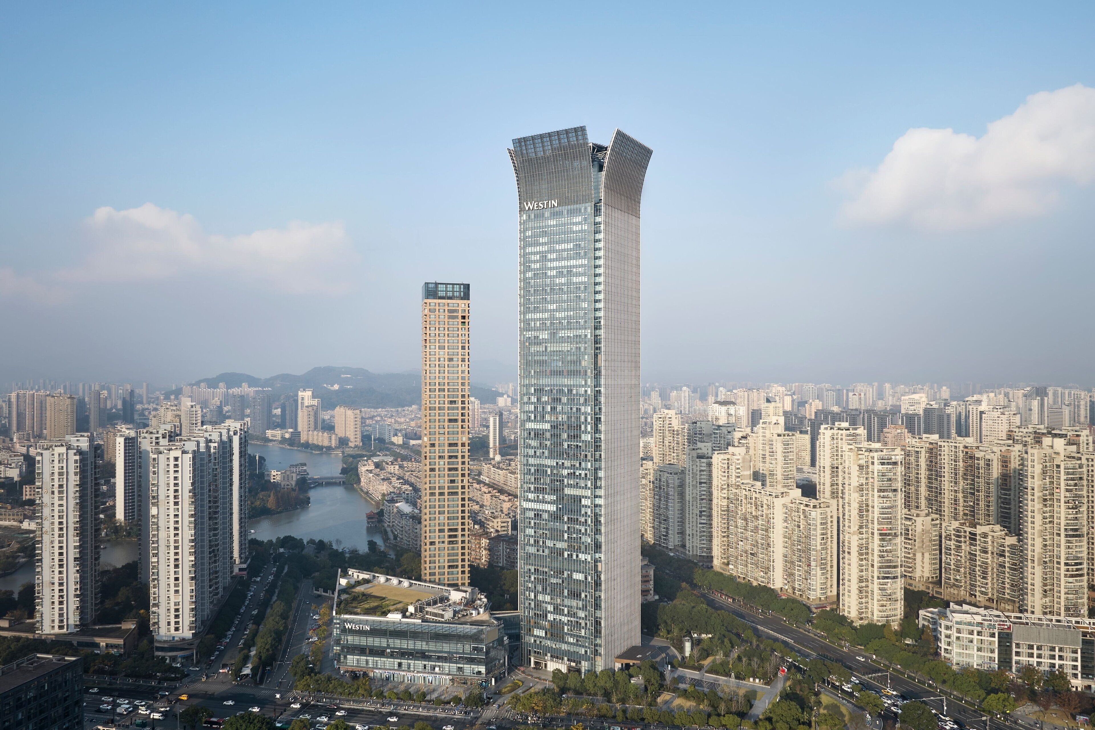 A high-rise building with a modern glass facade, surrounded by a dense urban environment with other high-rise buildings and a river in the background.