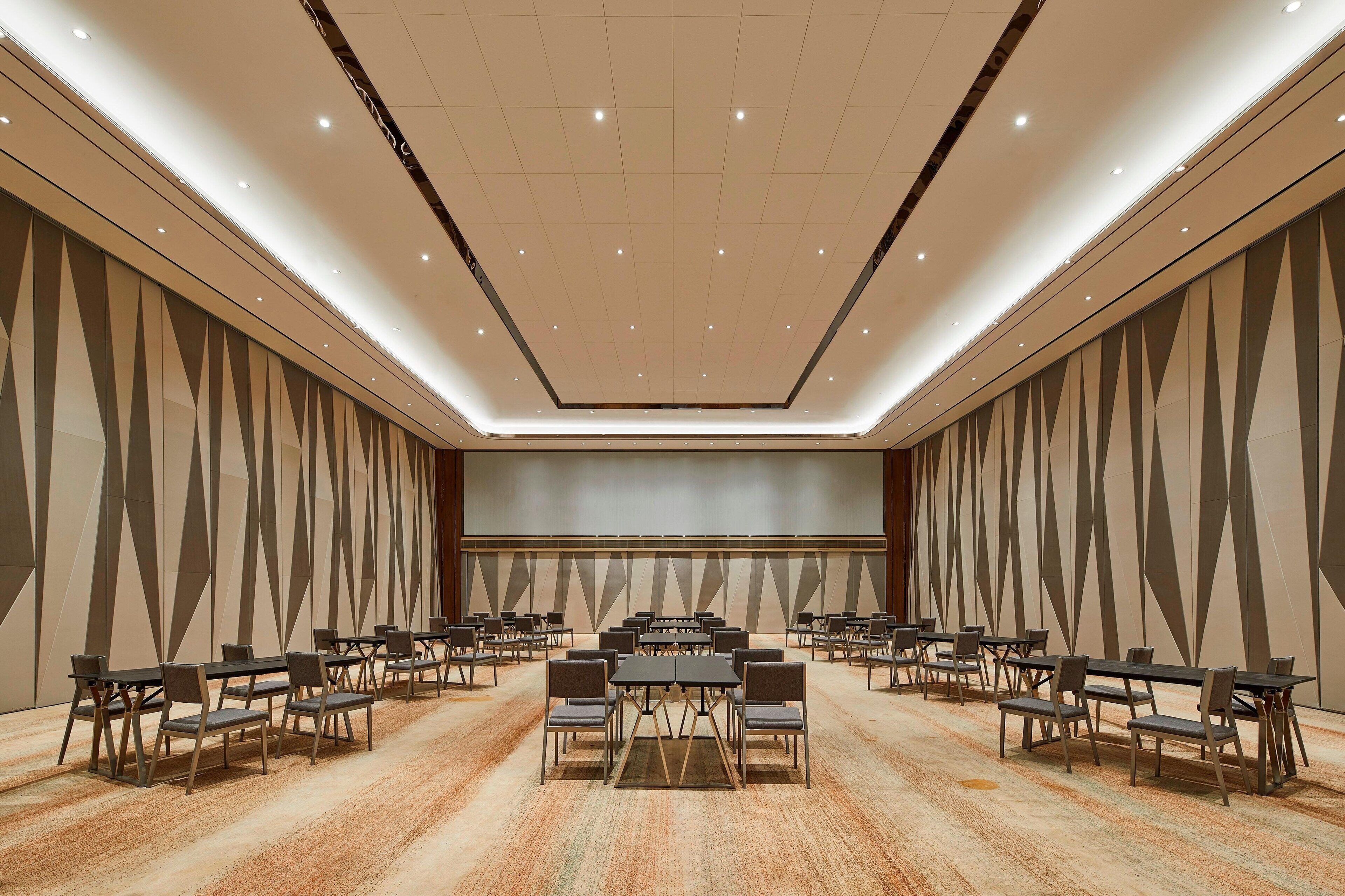 A conference room with multiple tables and chairs, a large screen at the front, and a patterned wall design.