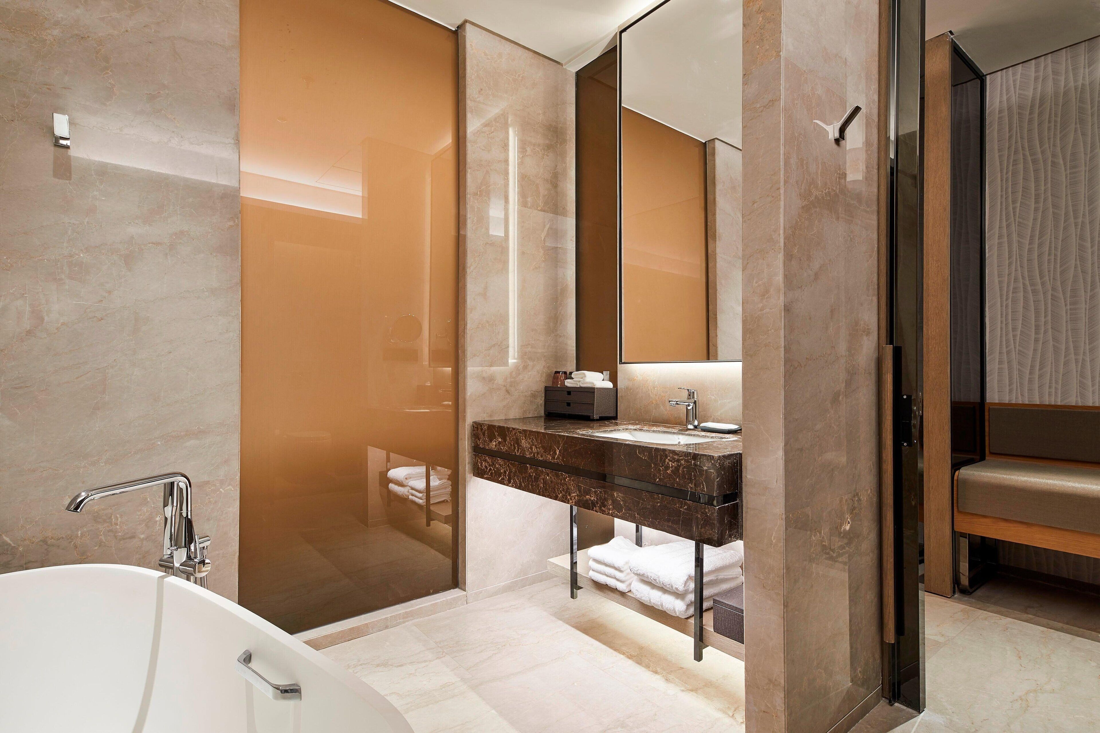 Een moderne badkamer met een vrijstaand bad, een douche met glazen wanden en een marmeren wastafel met wastafel en spiegel.