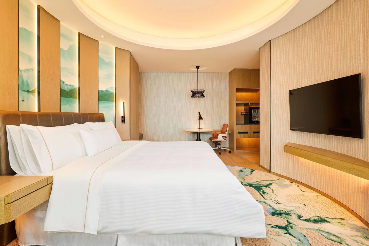 Ein Hotelzimmer mit einem großen Bett, einem flachbildfernseher an der Wand, einem kleinen Tisch mit einem Stuhl und einer dekorativen Wandverkleidung.