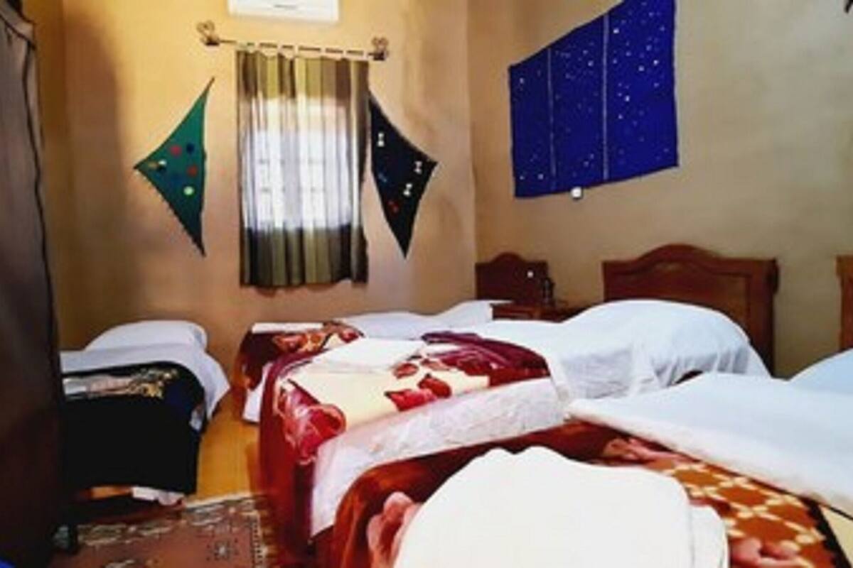 Una habitación con dos camas, cabecero de madera, una cortina y un tapiz con motivos de estrellas en la pared.