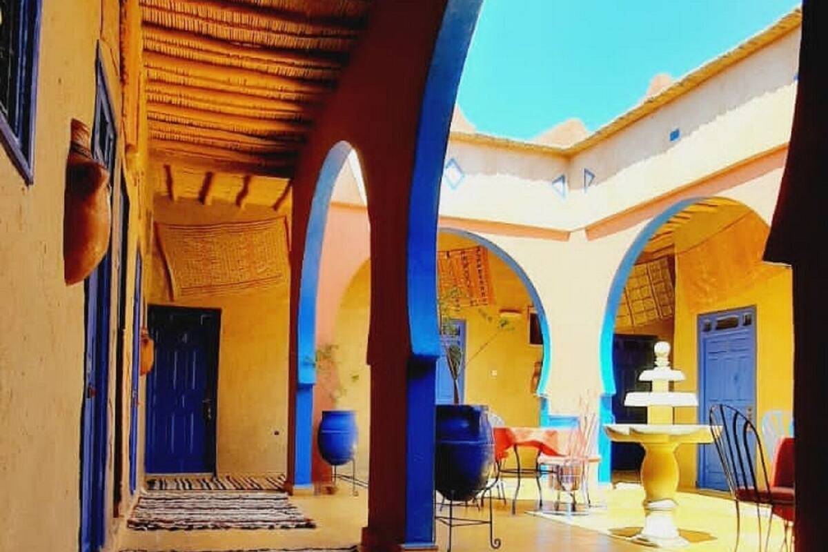 Un pasillo con suelo de baldosas, vigas de madera en el techo y arcos con marcos azules.