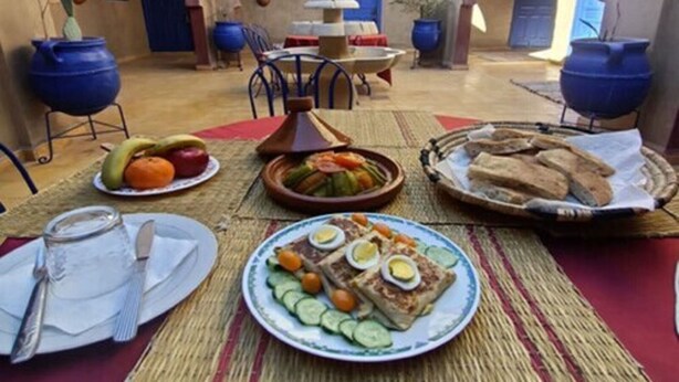 An outdoor dining area with a table set for a meal, surrounded by arches and potted plants. - Riad Tadarte Merzouga Desert Tours (Taouz)