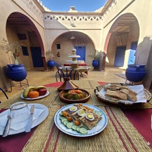 An outdoor dining area with a table set for a meal, surrounded by arches and potted plants. - Riad Tadarte Merzouga Desert Tours (Taouz)