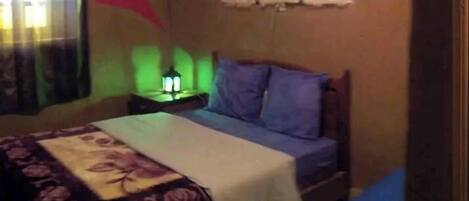 A bedroom with a bed, a nightstand, a wall-mounted lamp, and a window with curtains.