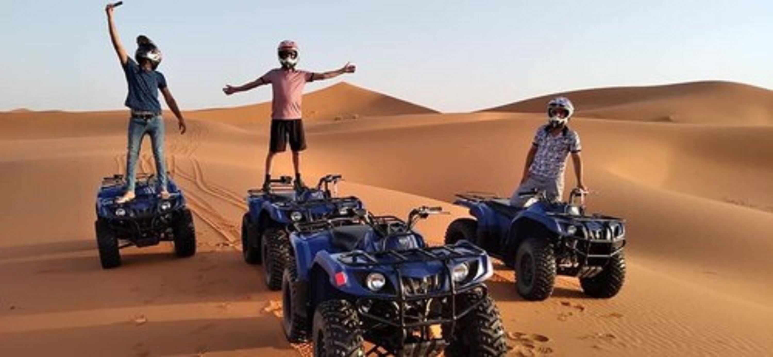 Tres personas conduciendo vehículos todo terreno en un desierto.