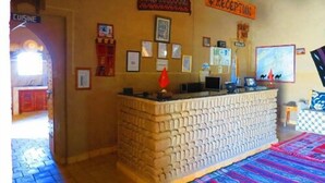 A reception area with a stone counter, framed pictures on the wall, and a 'RECEPTION' sign. - Riad Tadarte Merzouga Desert Tours (Taouz)