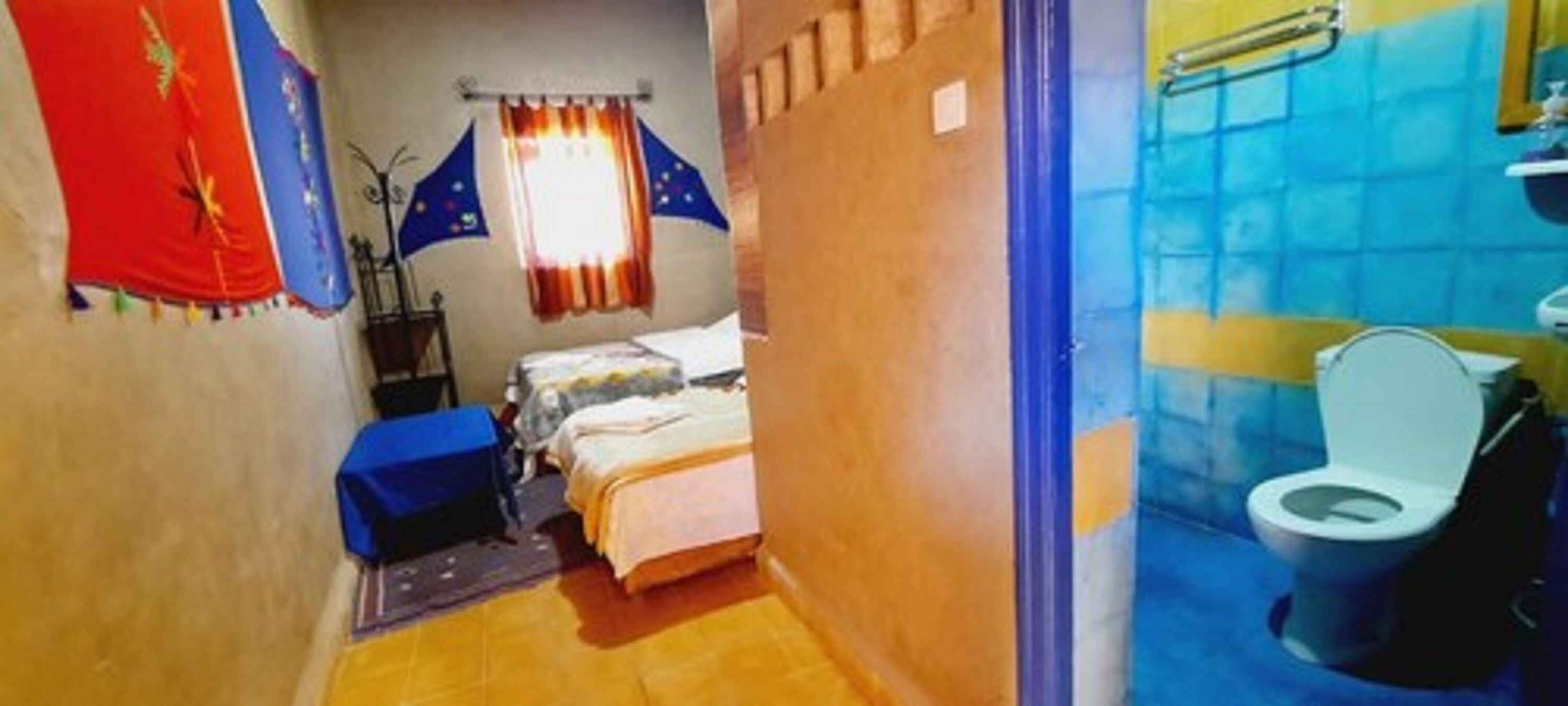 A narrow room with a bed, a small table, and a bathroom with a toilet.