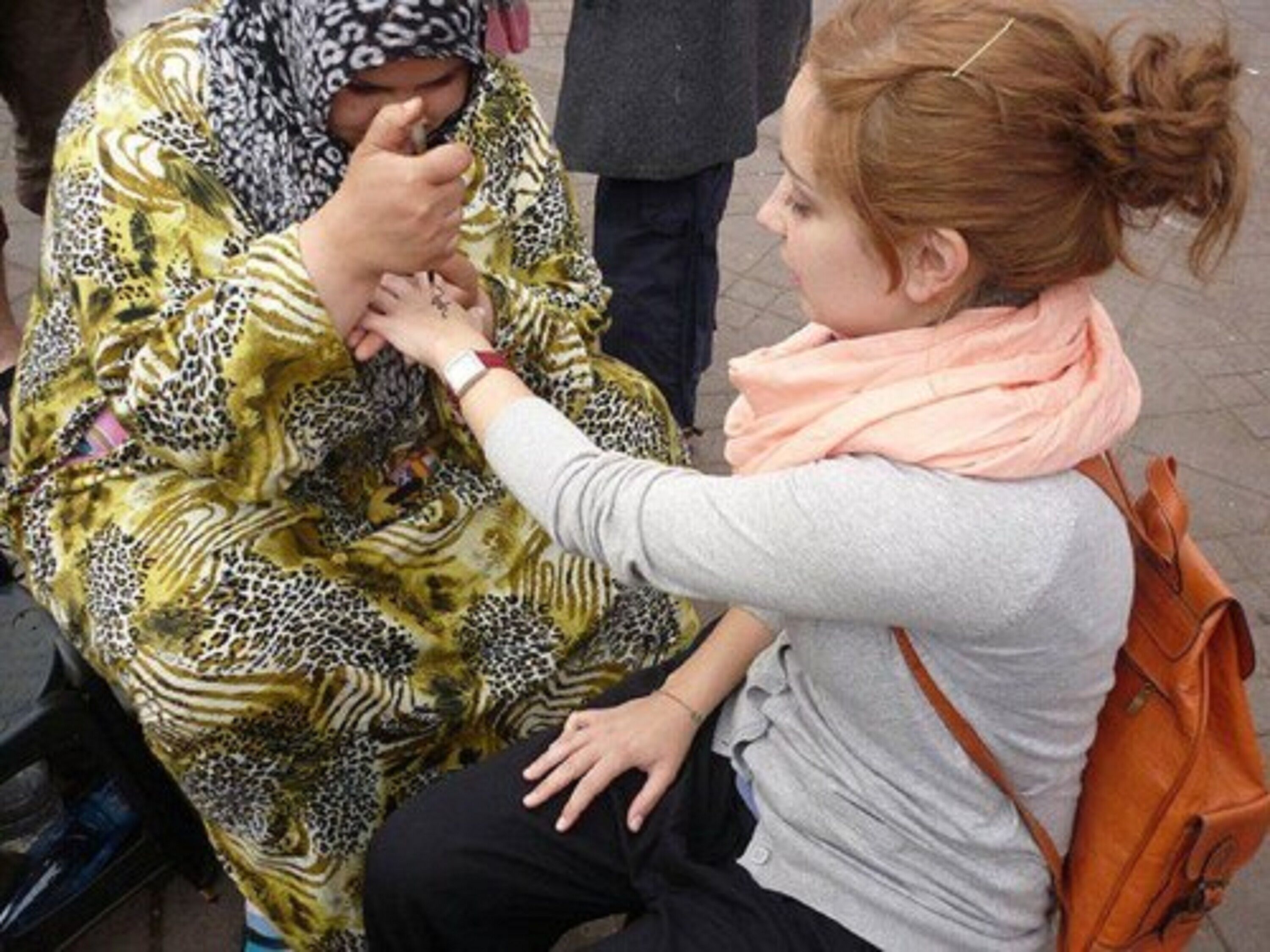 A person sitting on a bench, wearing a patterned garment and a headscarf, with a watch on their wrist.