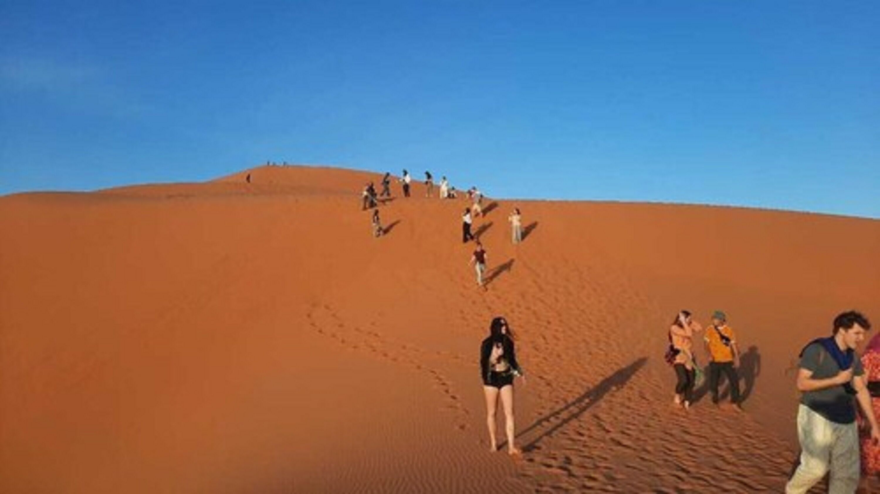 A group of people hiking up a large sand dune.