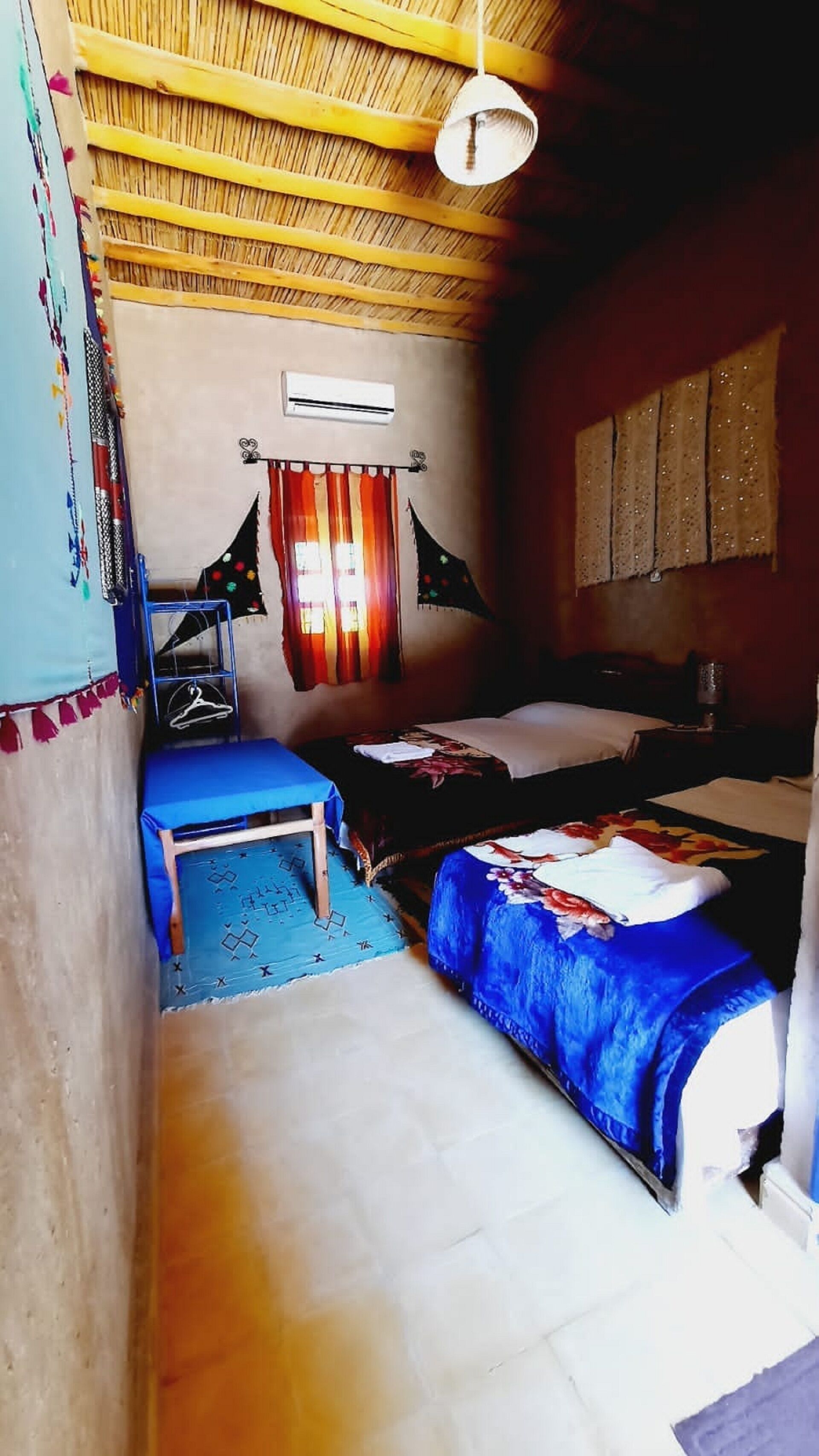 Una habitación con dos camas, un sofá azul, una mesita pequeña y una lámpara colgante.
