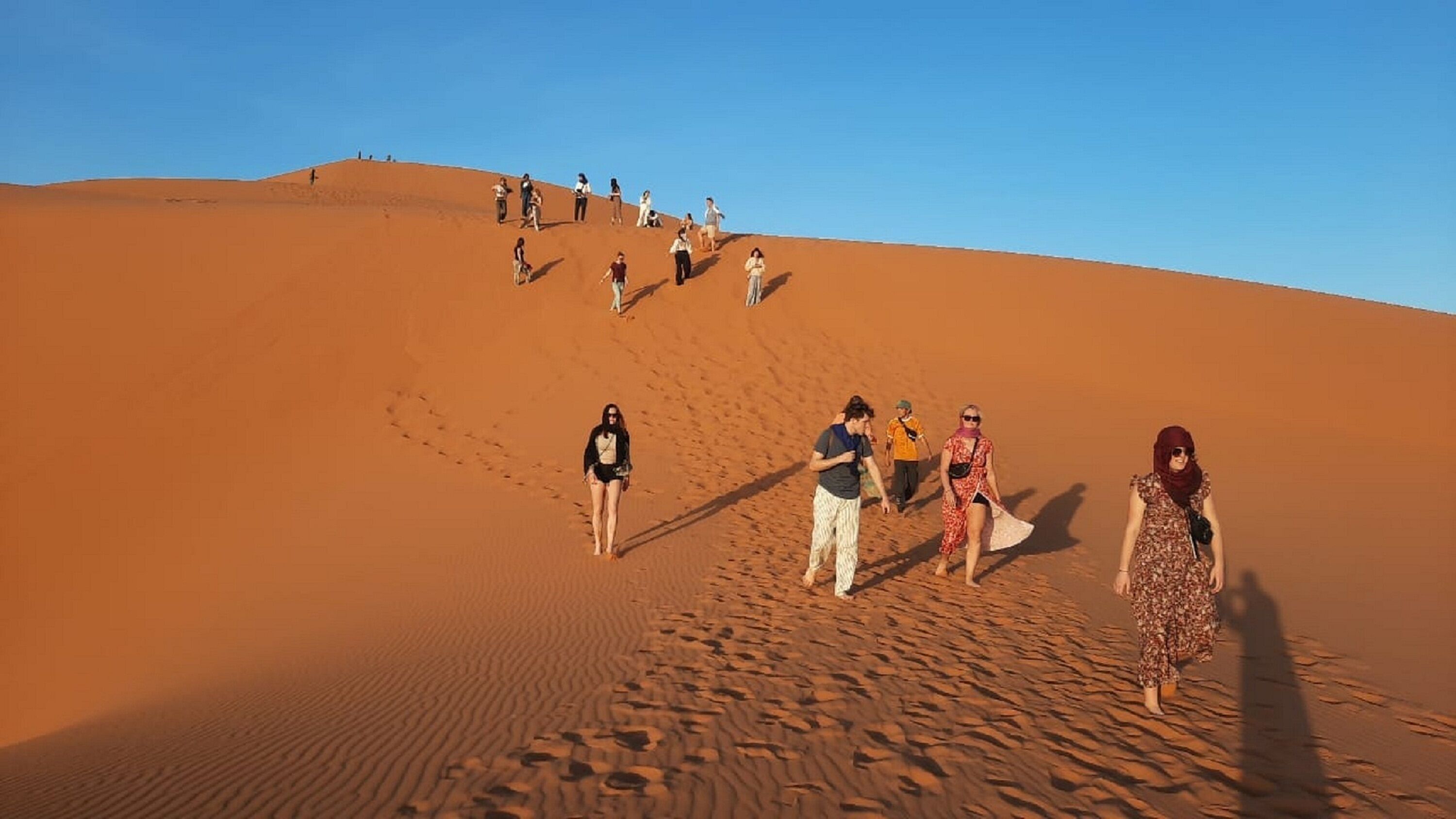 A desert landscape with sand dunes and a group of people walking.