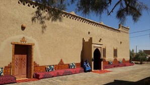 A traditional building with a flat facade, a central arched doorway, and a small tower-like structure on the right. - Riad Tadarte Merzouga Desert Tours (Taouz)