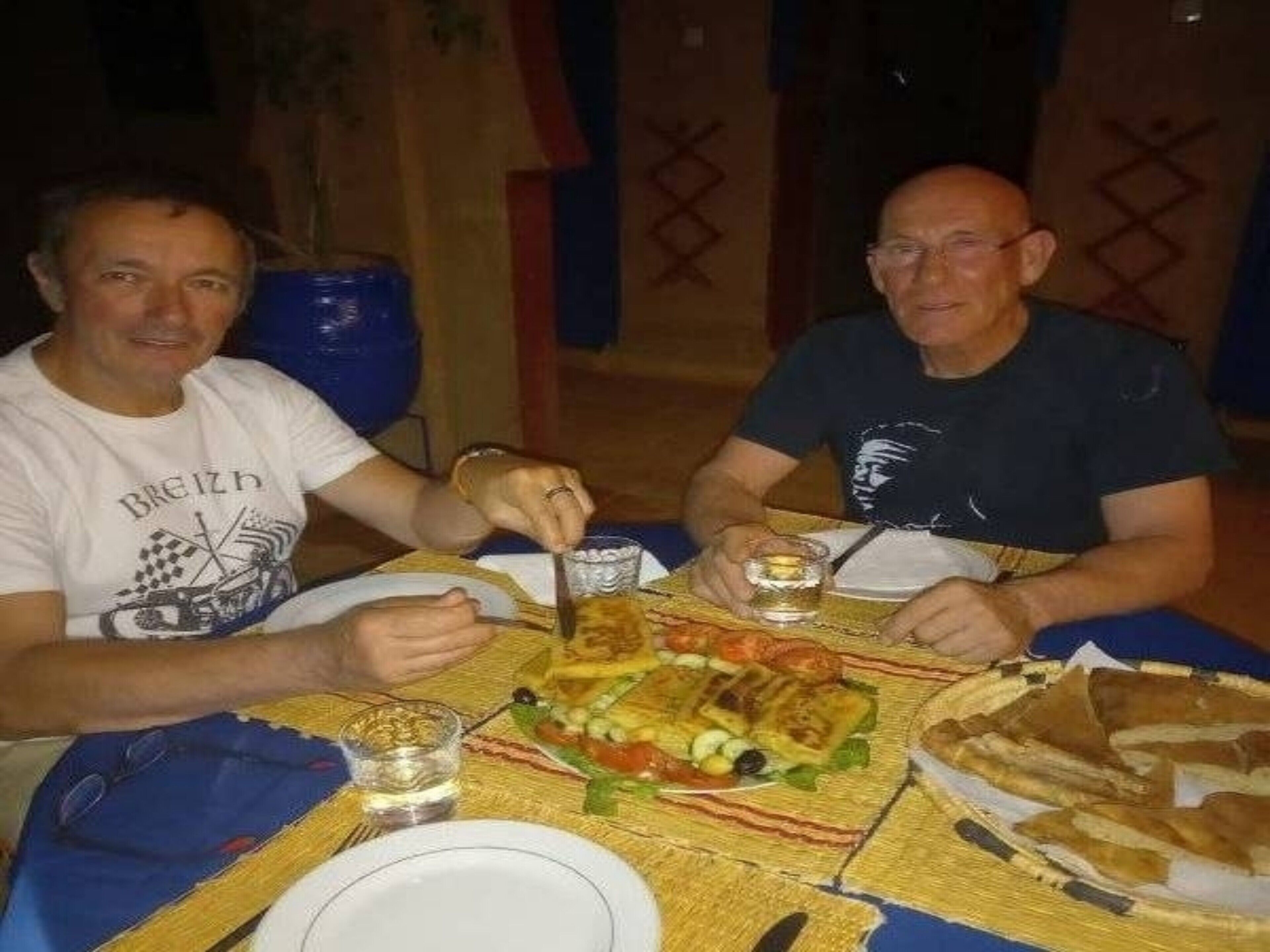 Zwei Personen essen an einem Tisch mit verschiedenen Speisen, darunter Pizza und Salat.