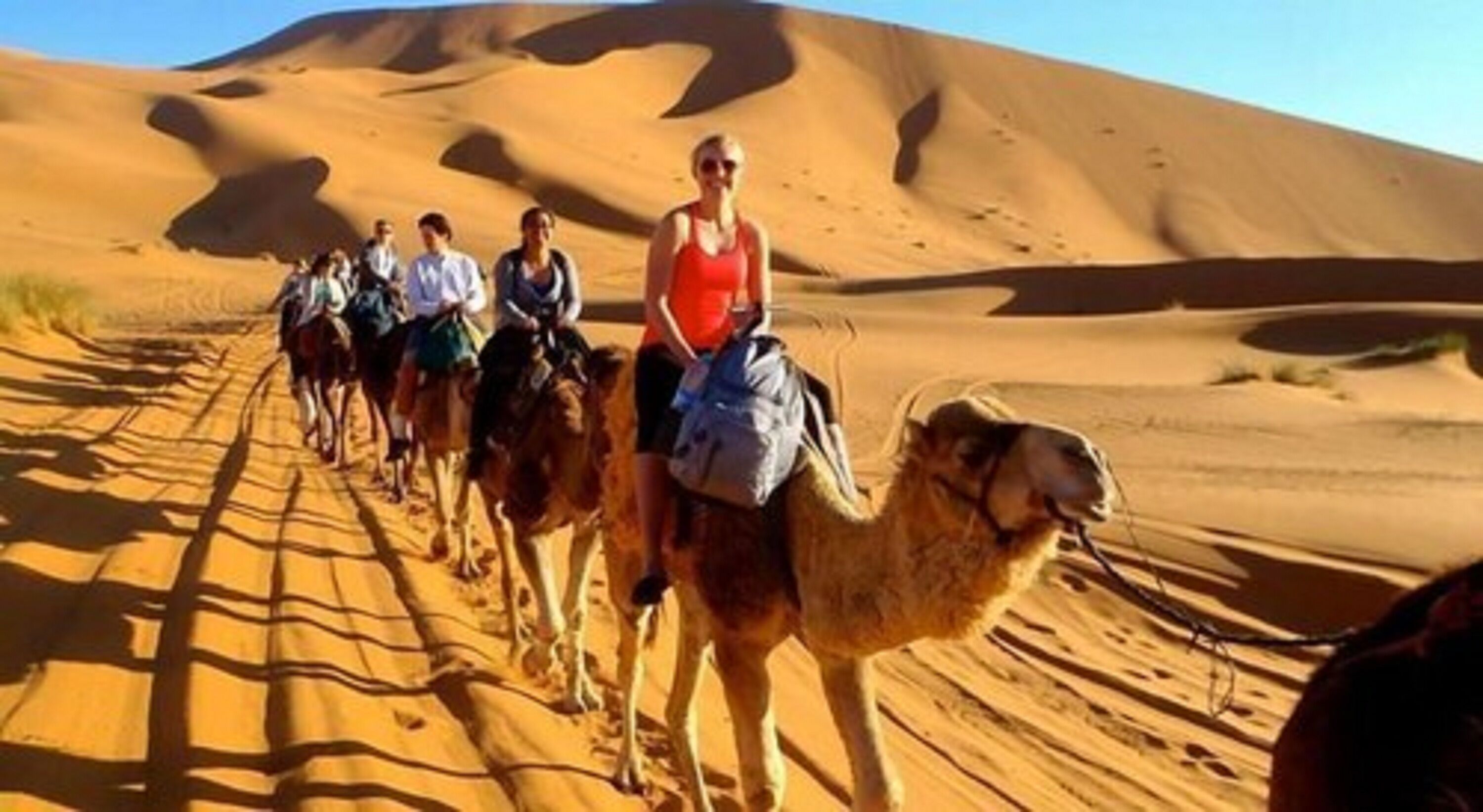 A group of people riding camels through a desert landscape with sand dunes.