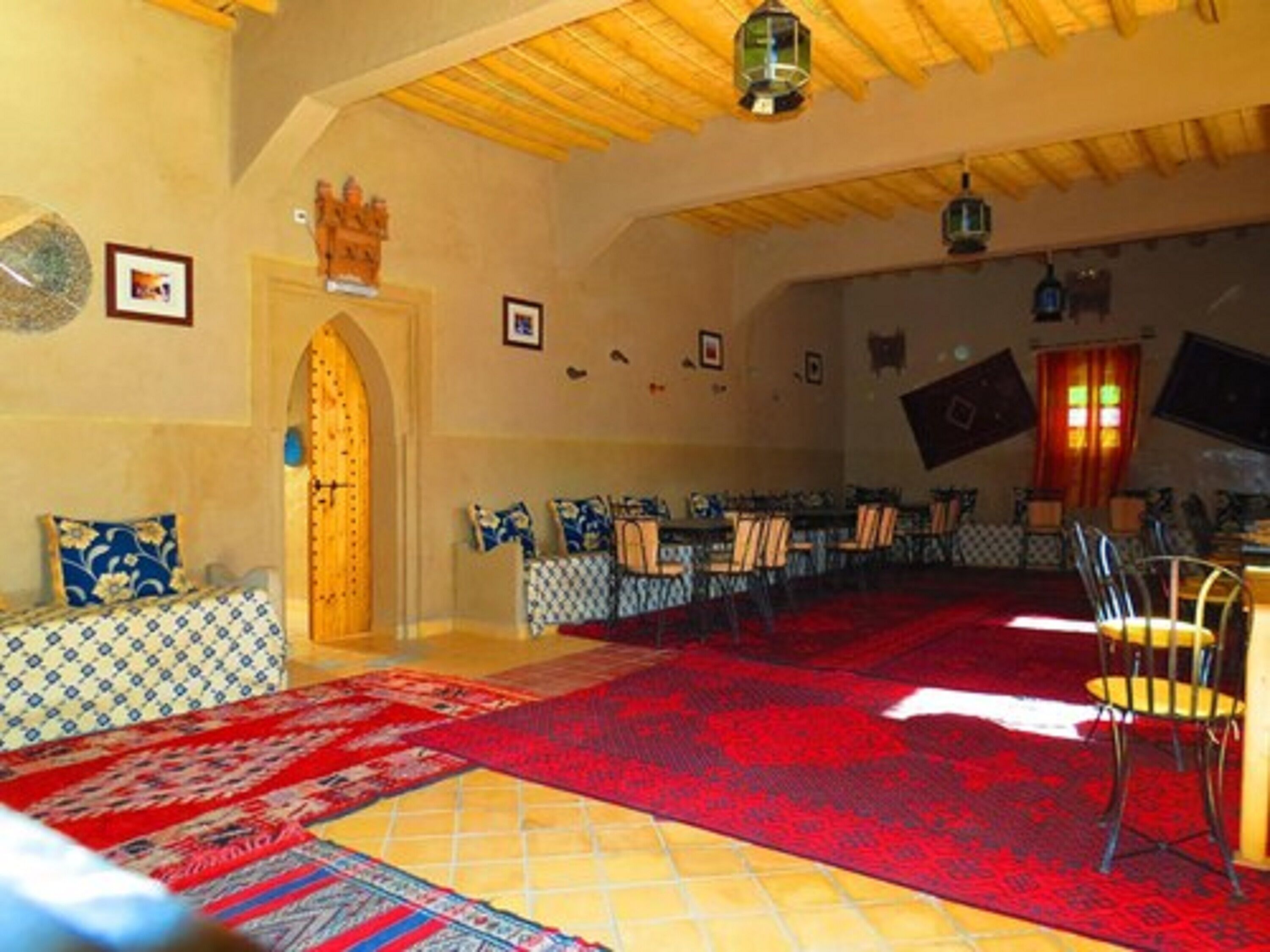 Une salle à manger spacieuse avec un plafond haut et des poutres en bois, comprenant une longue table entourée de chaises, un tapis à motifs et un arc décoratif.