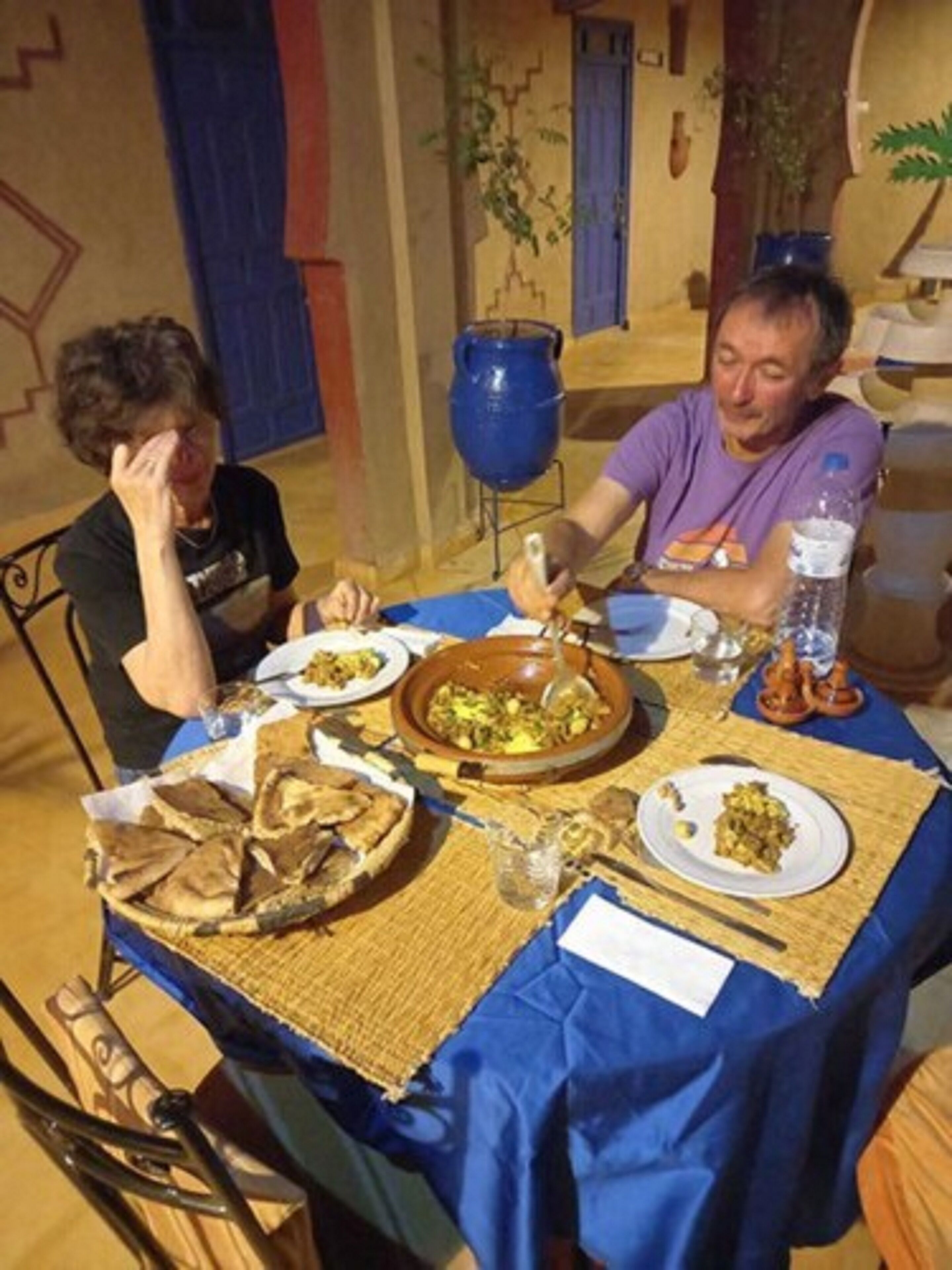 A dining table with plates of food, a blue tablecloth, and a blue pot.