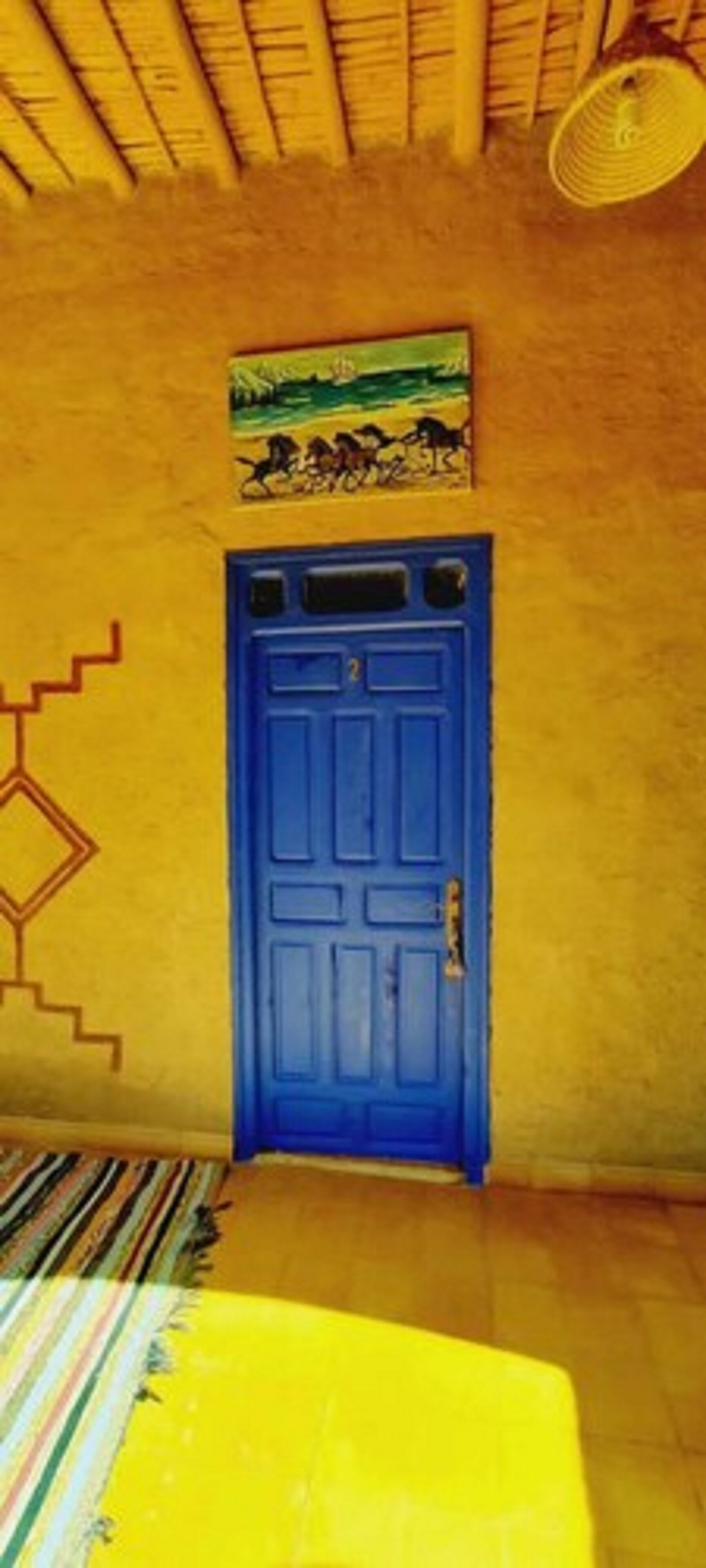 A room with a blue door, a yellow wall, and a patterned rug.