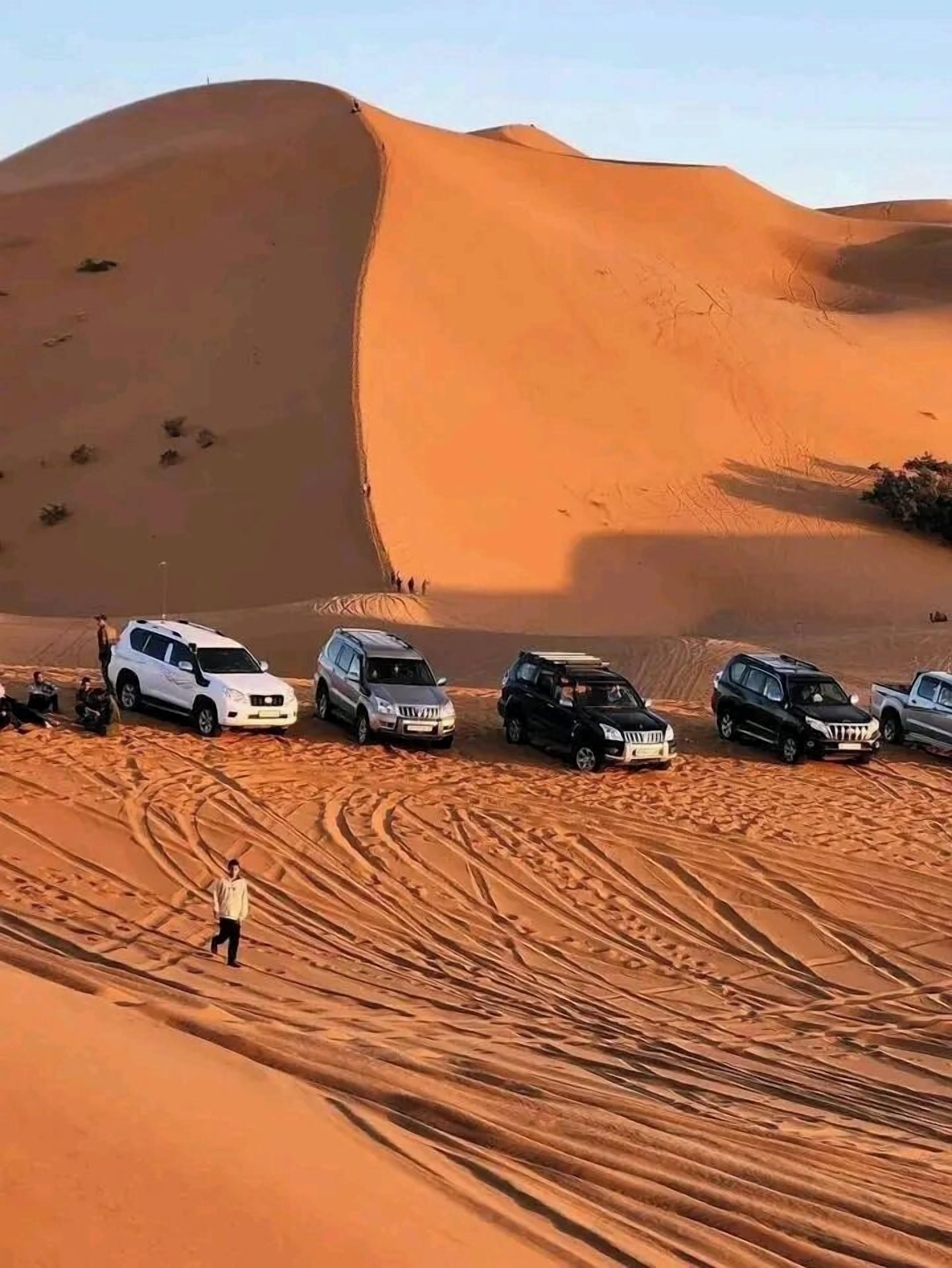 Un paysage désertique avec des dunes de sable et plusieurs véhicules tout-terrain garés sur le sable.
