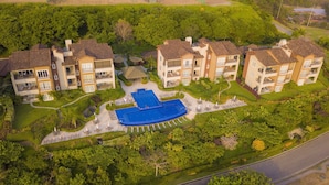 An aerial view of a residential complex with multiple two-story buildings, a central swimming pool, and well-maintained gardens. - Los Suenos Resort Miramar 5D (Jacó)