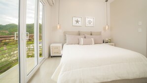 A bedroom with a large bed, a nightstand, a window with a view of greenery, and two wall-mounted lights. - Los Suenos Resort Miramar 5D (Jacó)