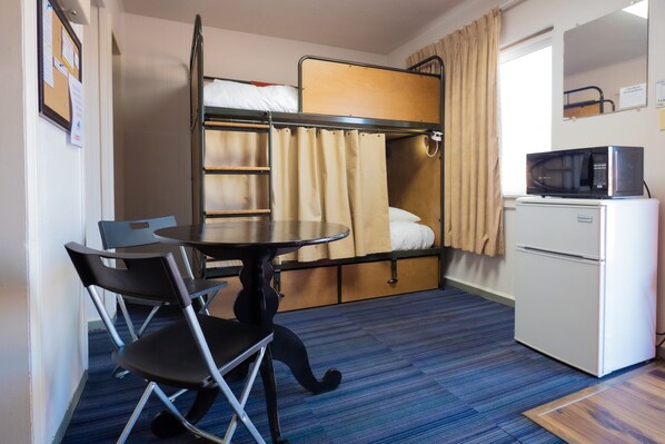 A compact hotel room with bunk beds, a small table with chairs, a microwave, and a refrigerator.