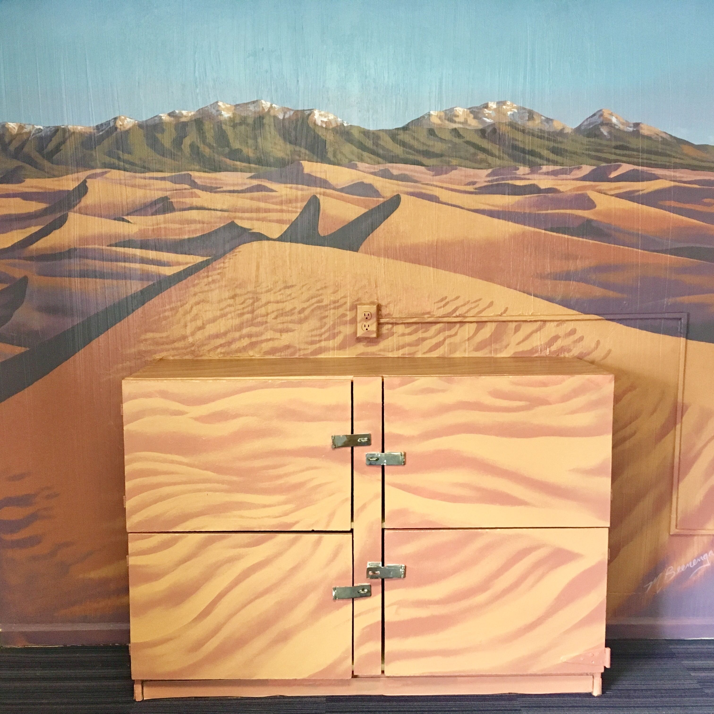 A room with a cabinet against a desert-themed mural.